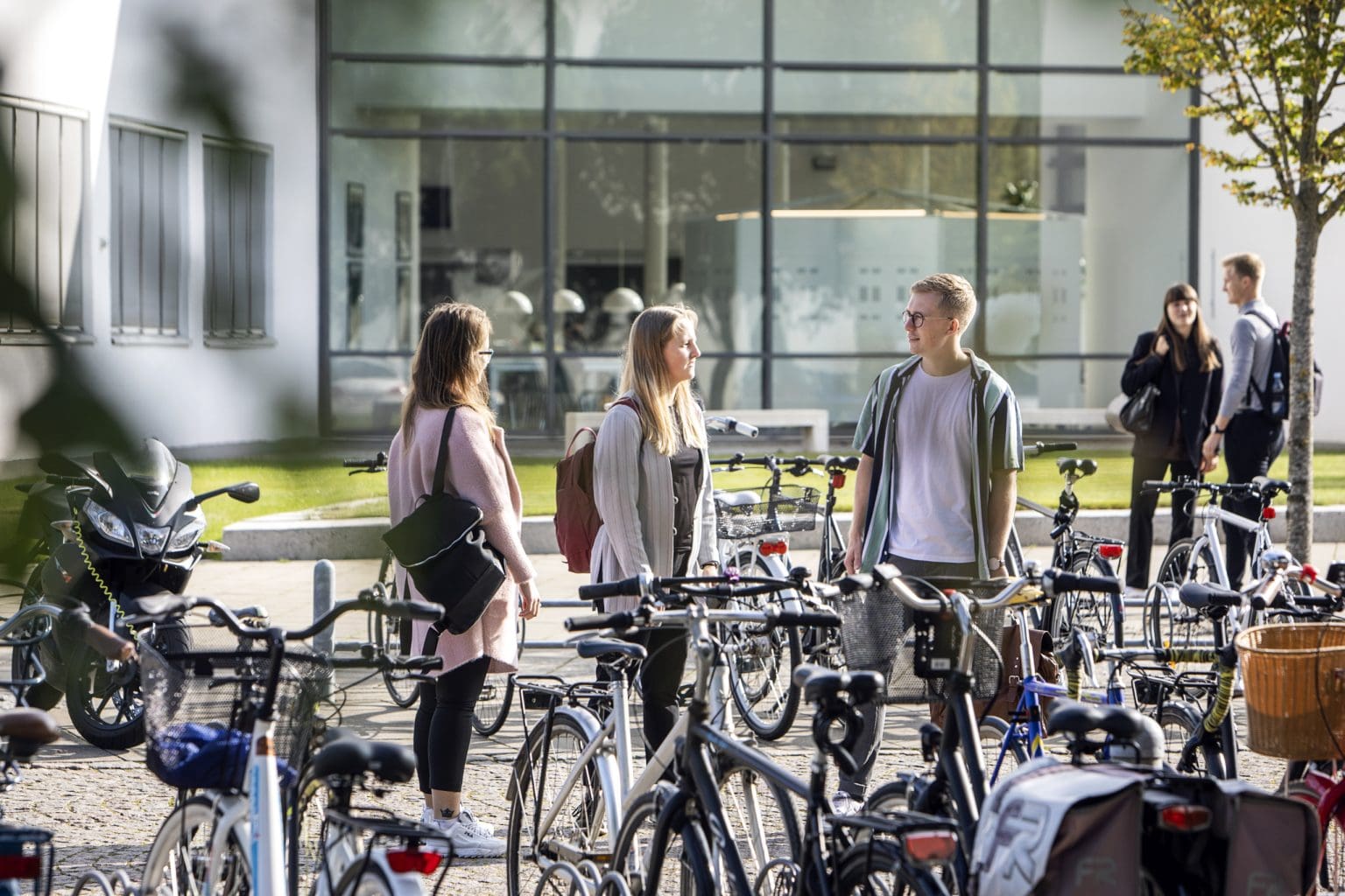 Et billede af tre unge mennesker der står og snakker ved en cykel parkeringsplads